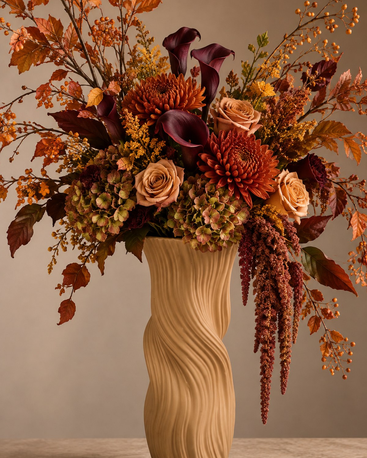 A tall wavy textured vase holding burgundy calla lilies, rust roses, orange dahlias and autumn branches.